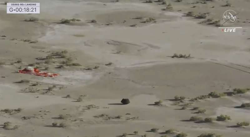 This image taken from video provided by NASA TV shows the capsule released by the Osiris-Rex spacecraft lying on the surface near the parachute after landing to Earth, Sunday Sept. 24 2023. Credit: NASA TV via AP
